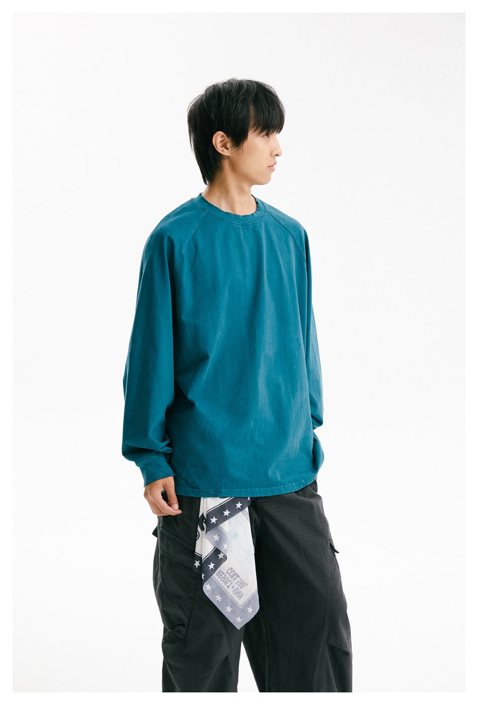 Side-facing model wearing a teal raglan long-sleeve shirt and dark cargo trousers.