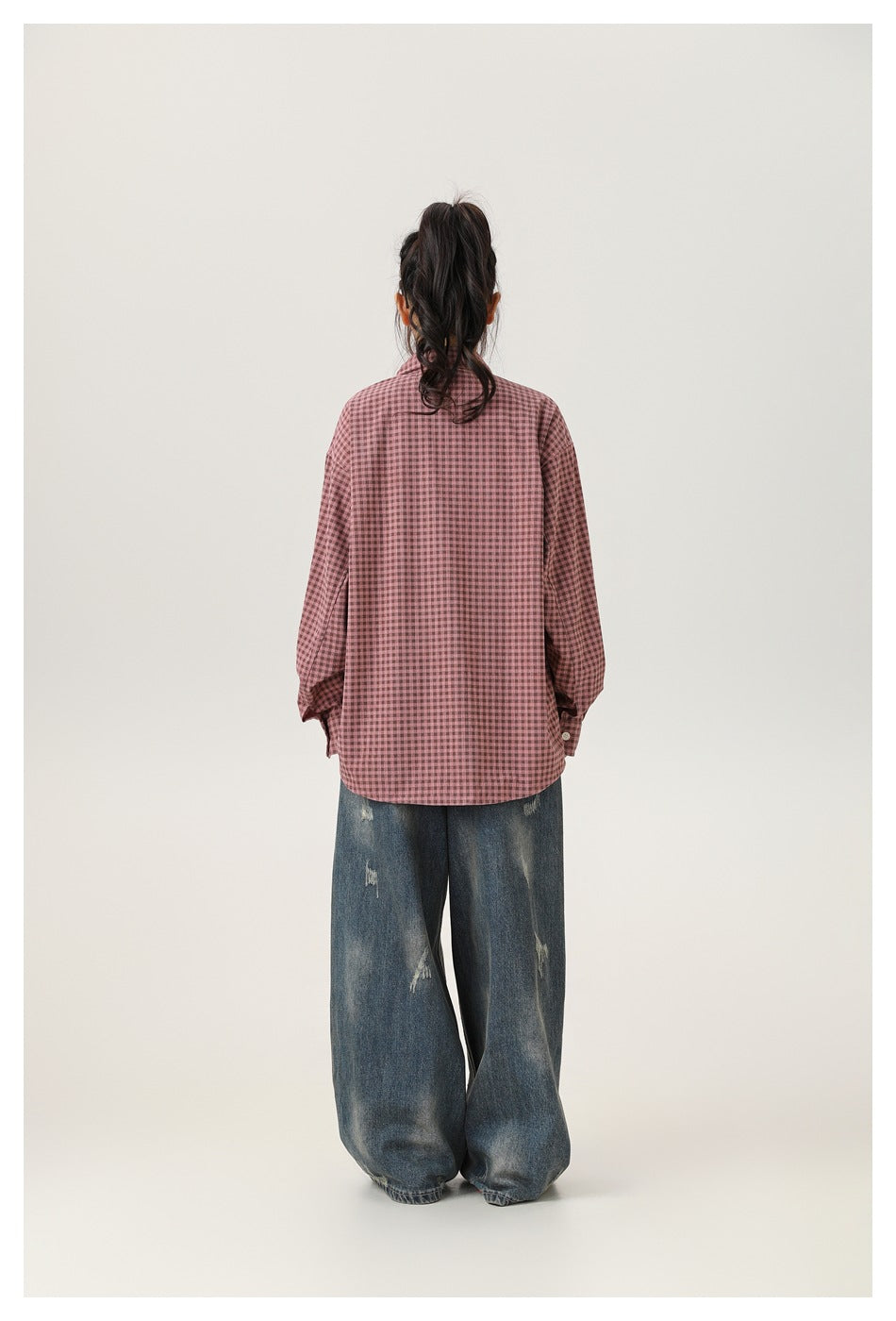 Back view of a model wearing a dusty rose and dark checked button-up shirt with oversized sleeves and loose jeans.