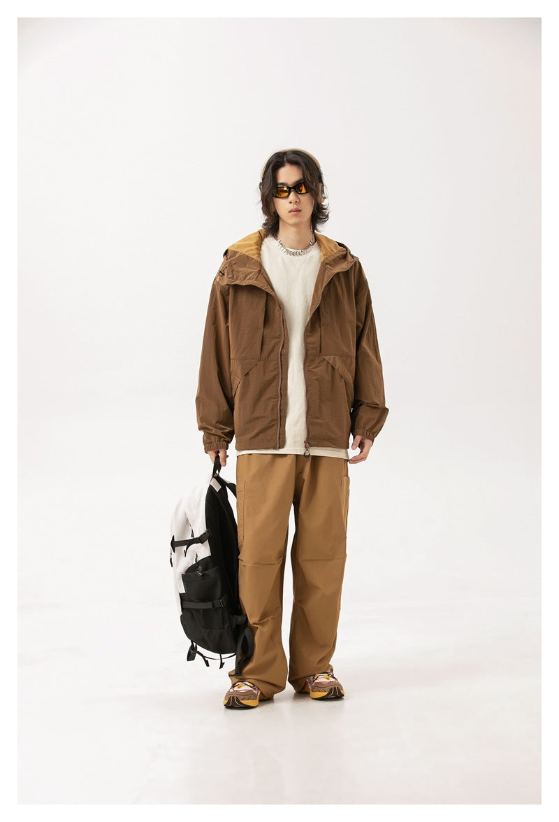 Full-length model wearing a brown hooded zip jacket, tan trousers and carrying a backpack.