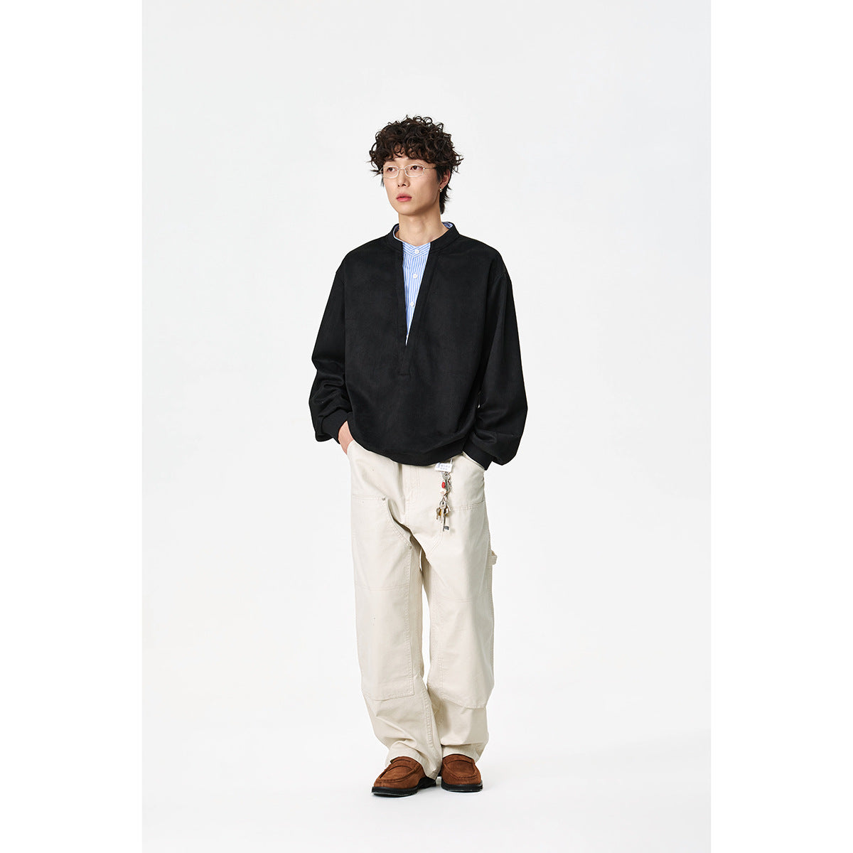 Model wearing a black oversized pullover with a split V neckline over a blue striped shirt.