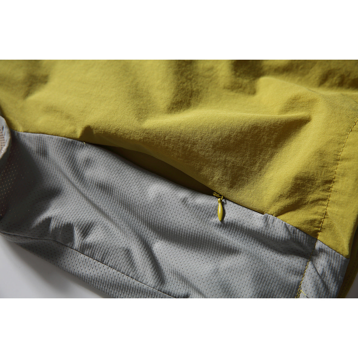 Close-up of the vest's mustard fabric, gray mesh lining, and a small zipper.