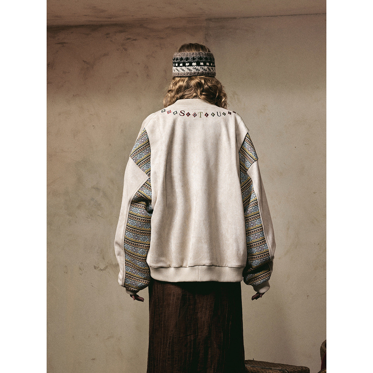 Back view of a model wearing an ivory jacket with colorful geometric-patterned sleeves and embroidered lettering.