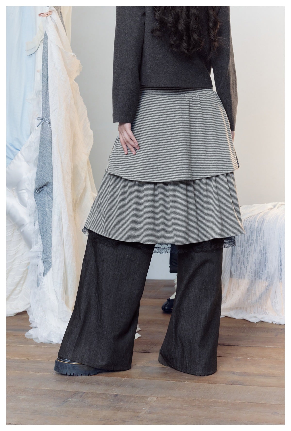 Angled back view of a model wearing a gray striped tiered skirt over wide black pants.