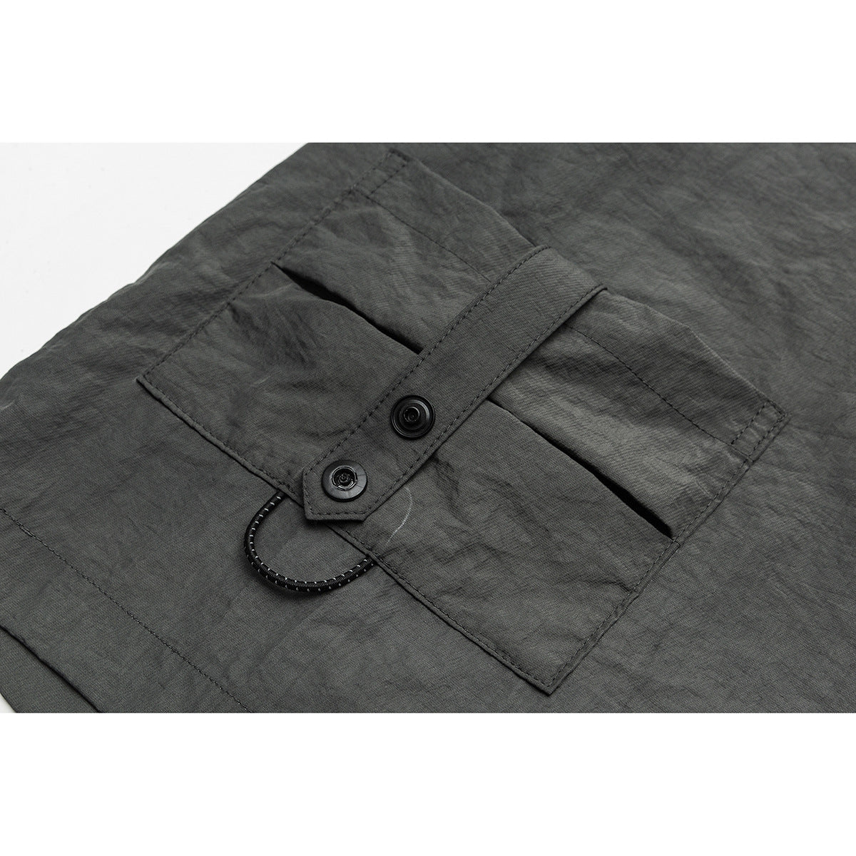 Close-up of a charcoal-gray garment pocket with a buttoned tab and a looped cord detail.