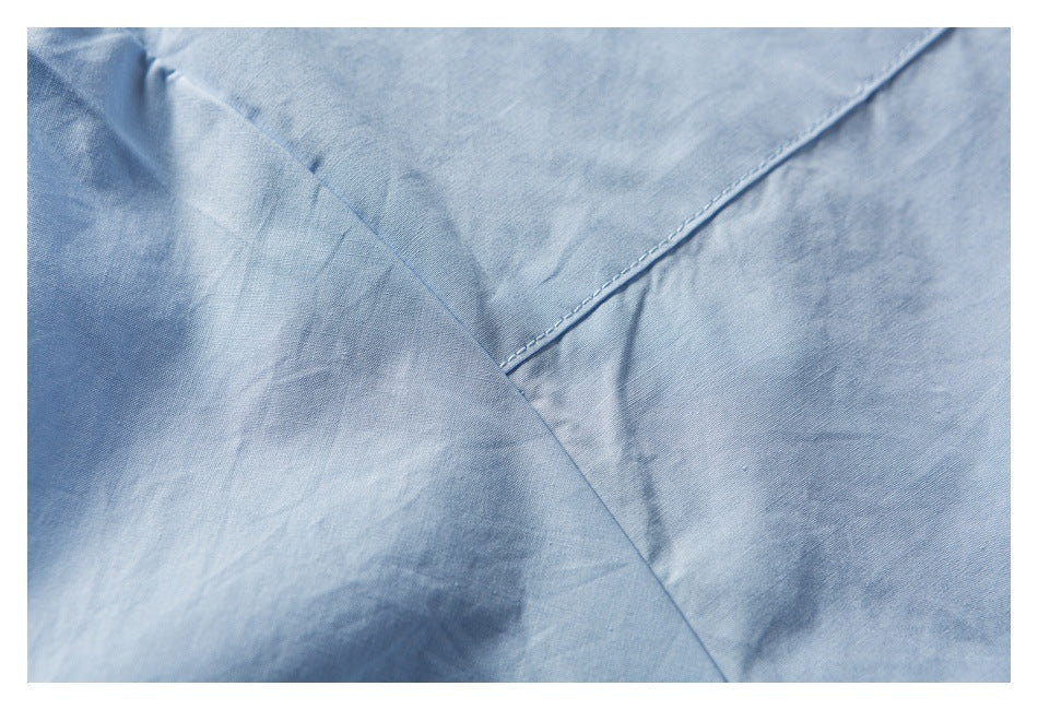 Close-up of light blue garment fabric with a diagonal stitched seam and overlapping fabric panels.