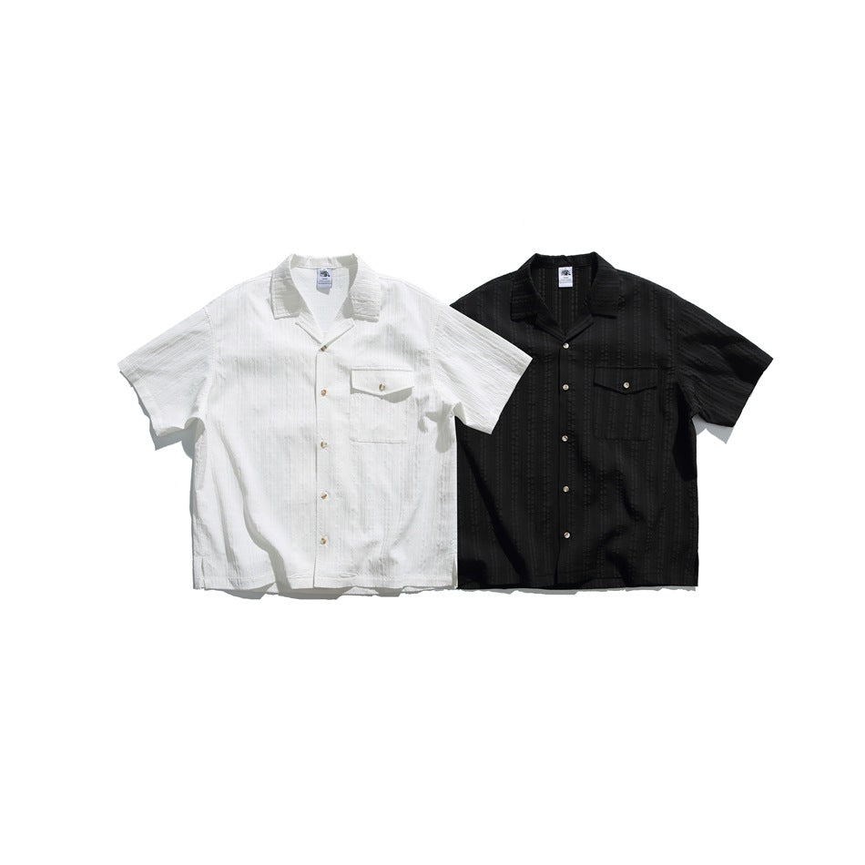 White and black short-sleeve shirts shown from the front, each with a notched collar, button closure, and flap chest pocket.