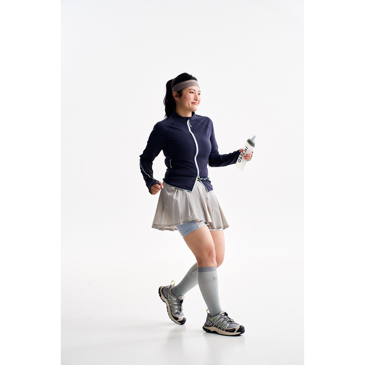 Model wearing a navy zip-up athletic jacket and gray pleated skirt with built-in shorts.
