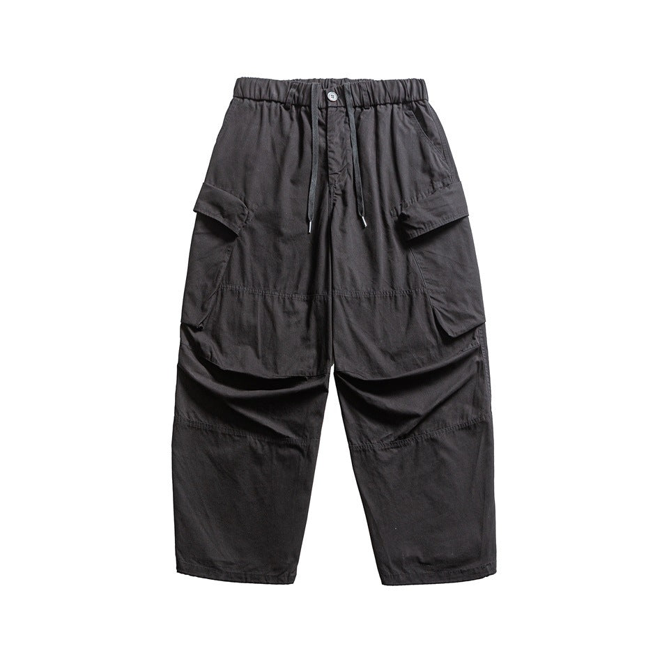 Front view of dark charcoal cargo pants with an elastic drawstring waist, large flap pockets and paneled legs.
