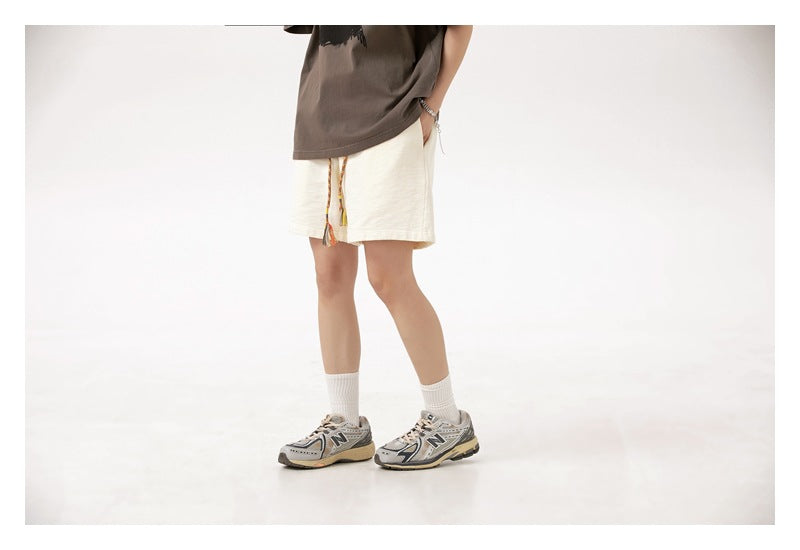 Three-quarter view of a model wearing cream loose shorts with a colorful tasseled drawstring.