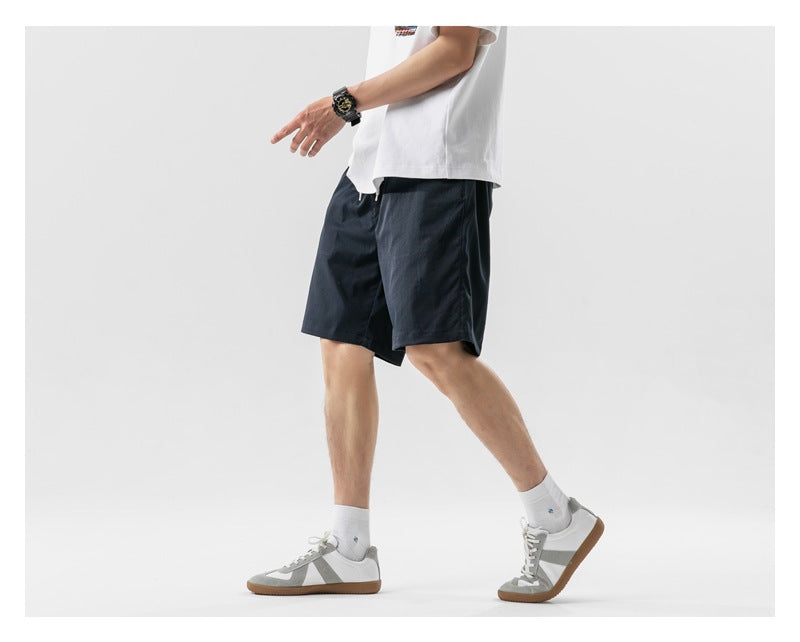 Cropped view of a model wearing dark navy shorts with a white T-shirt, shown walking from the side.
