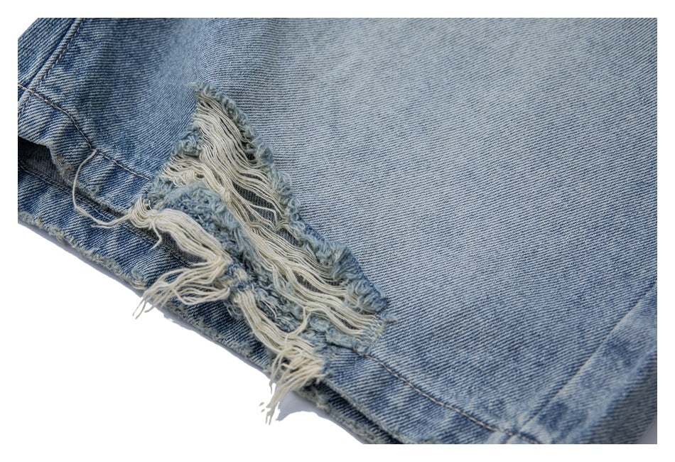 Close-up of a heavily distressed tear with loose white threads on light blue jeans.