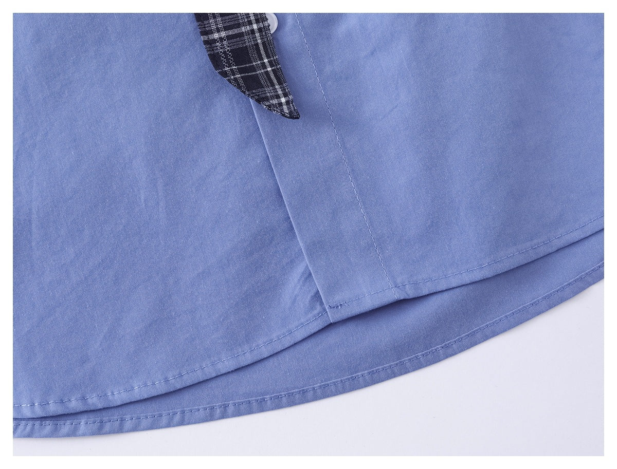 Close-up of a light blue shirt hem with visible stitching and a glimpse of plaid fabric.
