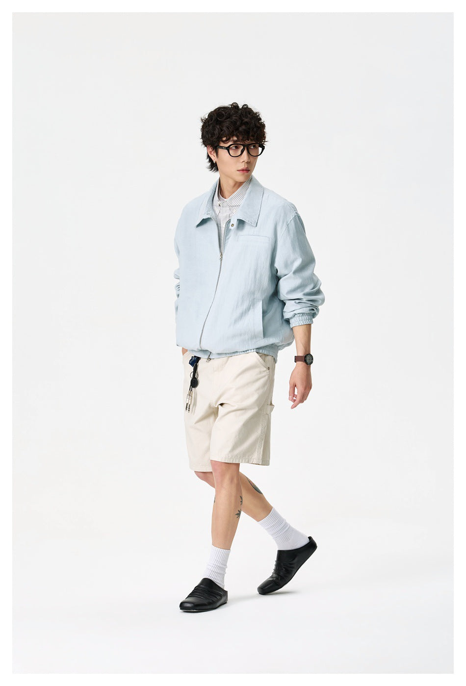 Full-length view of a model in a light blue zip jacket with beige shorts, white socks and black slip-on shoes
