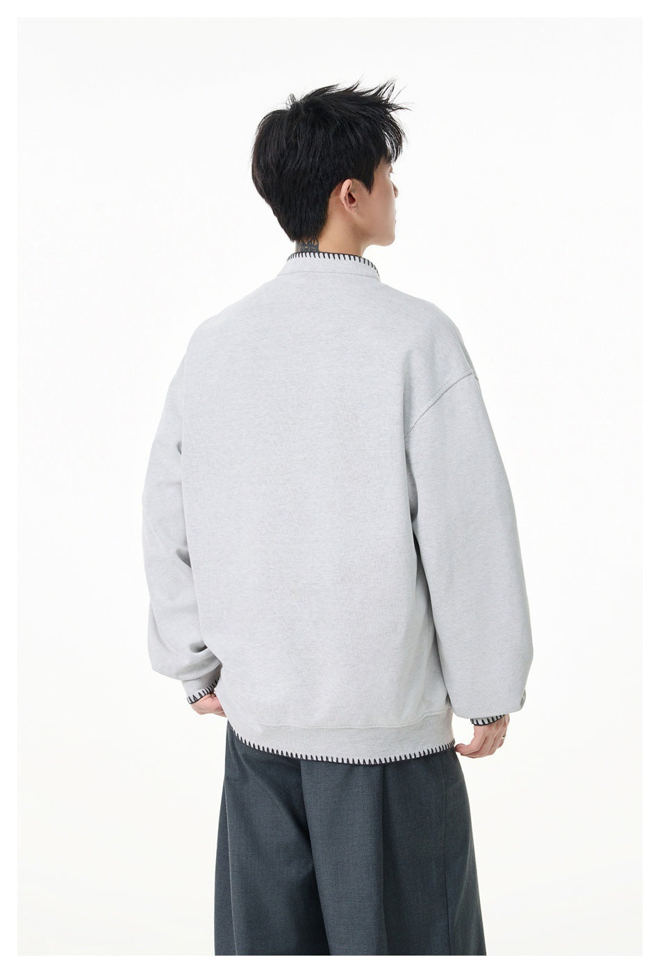 Back view of a model wearing a light gray oversized pullover with black contrast stitching at the collar, cuffs and hem.