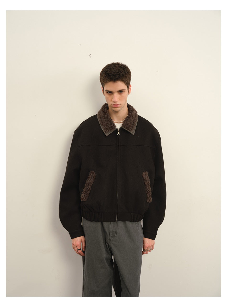 Front view of a model in a black zip jacket with brown textured collar and pocket trim, and gray jeans.