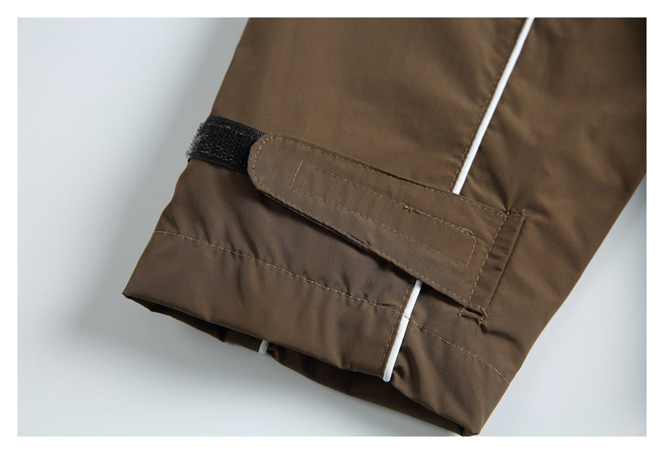 Close-up of a brown jacket sleeve cuff with an adjustable hook-and-loop strap and white piping.