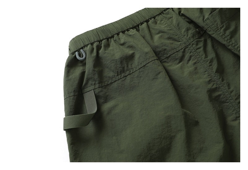 Close-up of dark olive shorts showing the elastic waistband, drawcord loop, and side webbing tab.