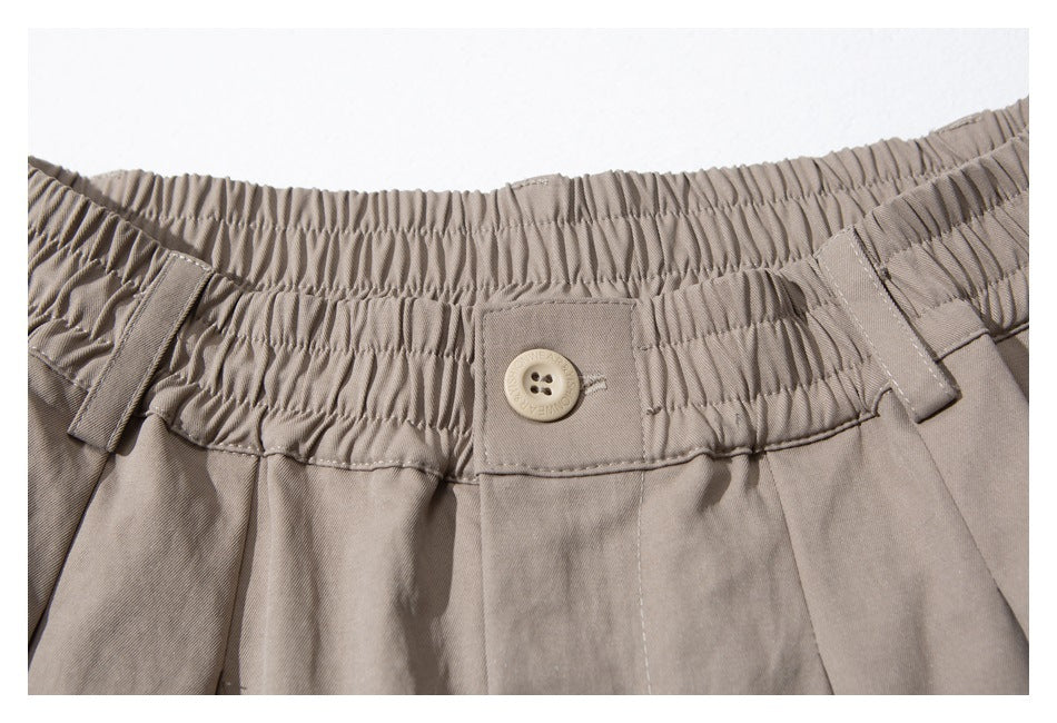 Close-up of taupe trousers with a gathered elastic waistband, belt loops, and a matching button.