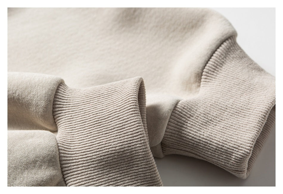 Close-up of a cream hoodie sleeve and body, showing ribbed cuffs and fabric texture.