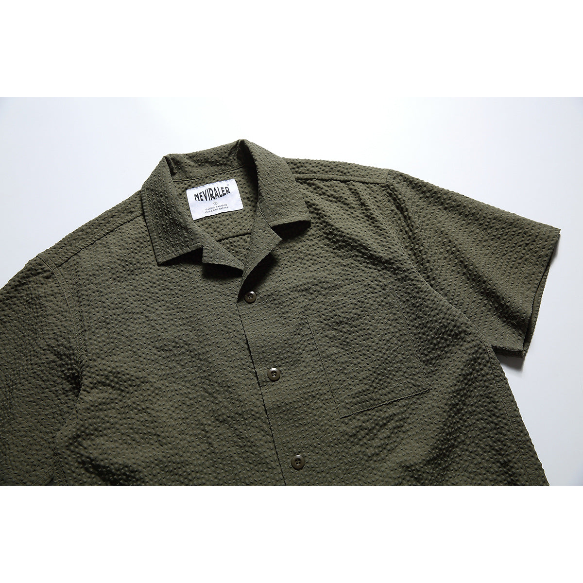 Olive short-sleeve button-up shirt with a textured surface, pointed collar, and single chest pocket, shown from the front.