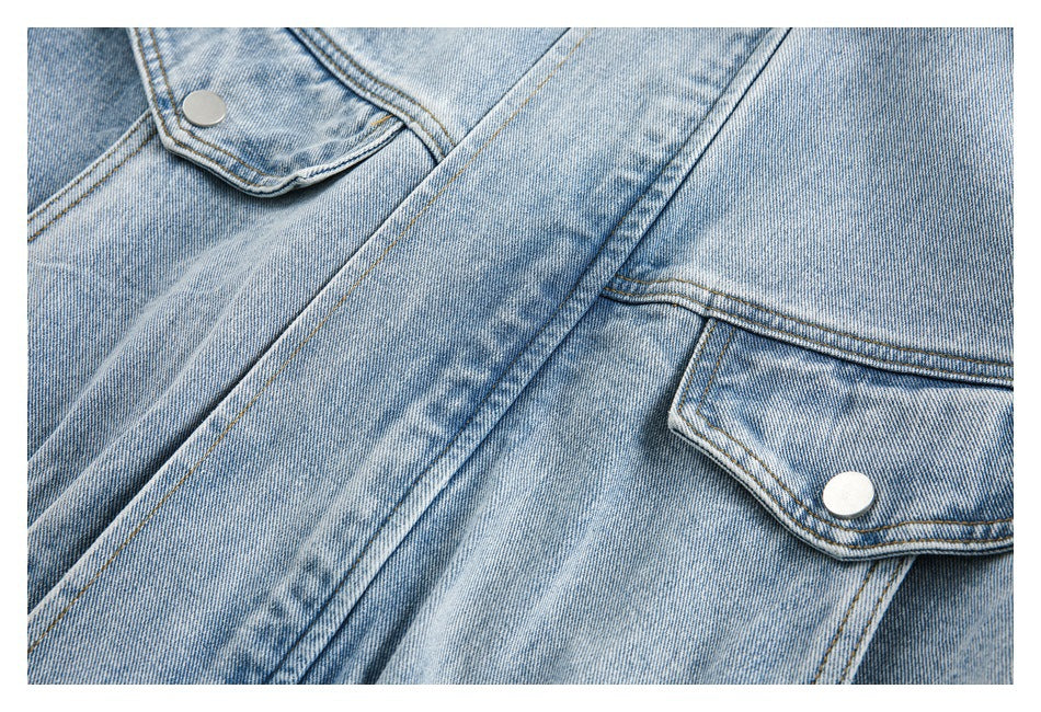 Close-up of a light blue denim jacket with flap pockets, silver snaps and contrast stitching.