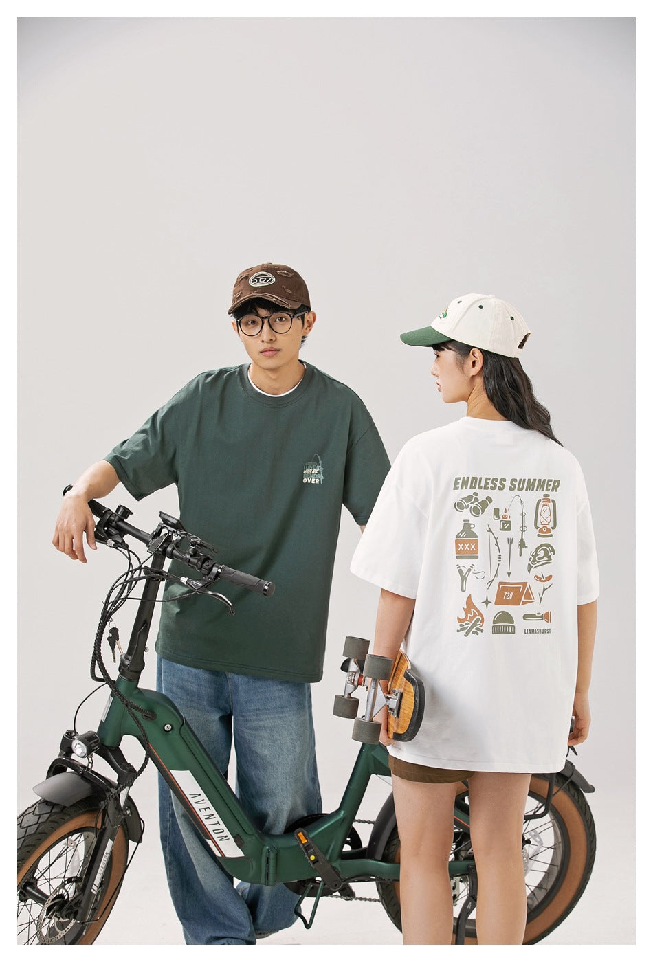 Two models wear oversized graphic T-shirts: a dark green shirt shown from the front and a white shirt shown from the back.