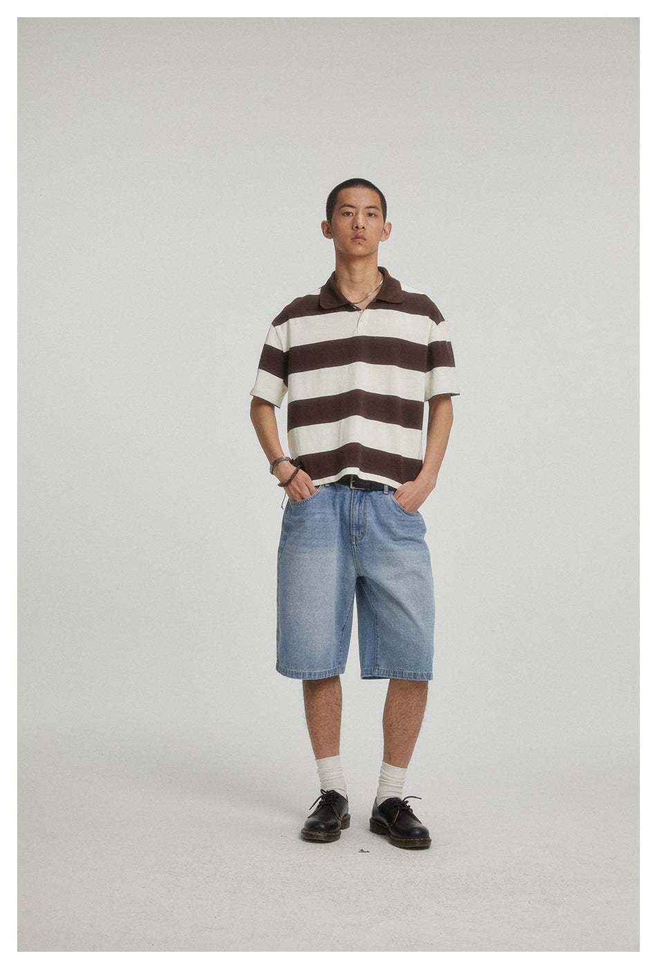 Front view of a model in a brown-and-cream striped polo shirt and light blue denim shorts.