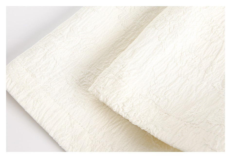 Close-up of overlapping ivory garment panels with textured floral fabric and stitched edges.