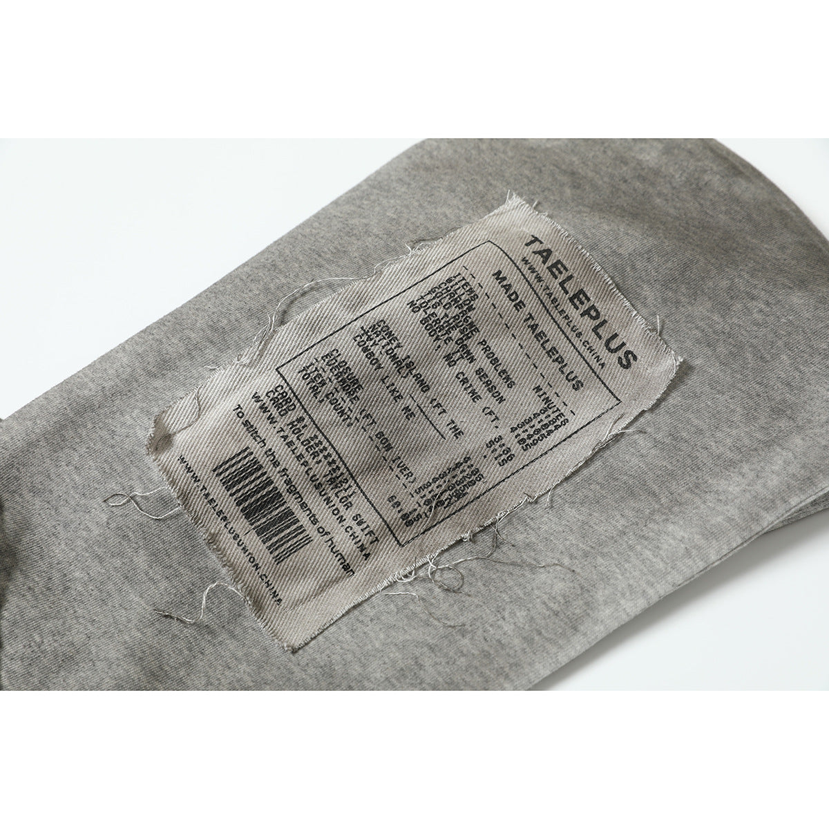 Close-up of a sewn garment label with English text and a barcode on gray fabric.