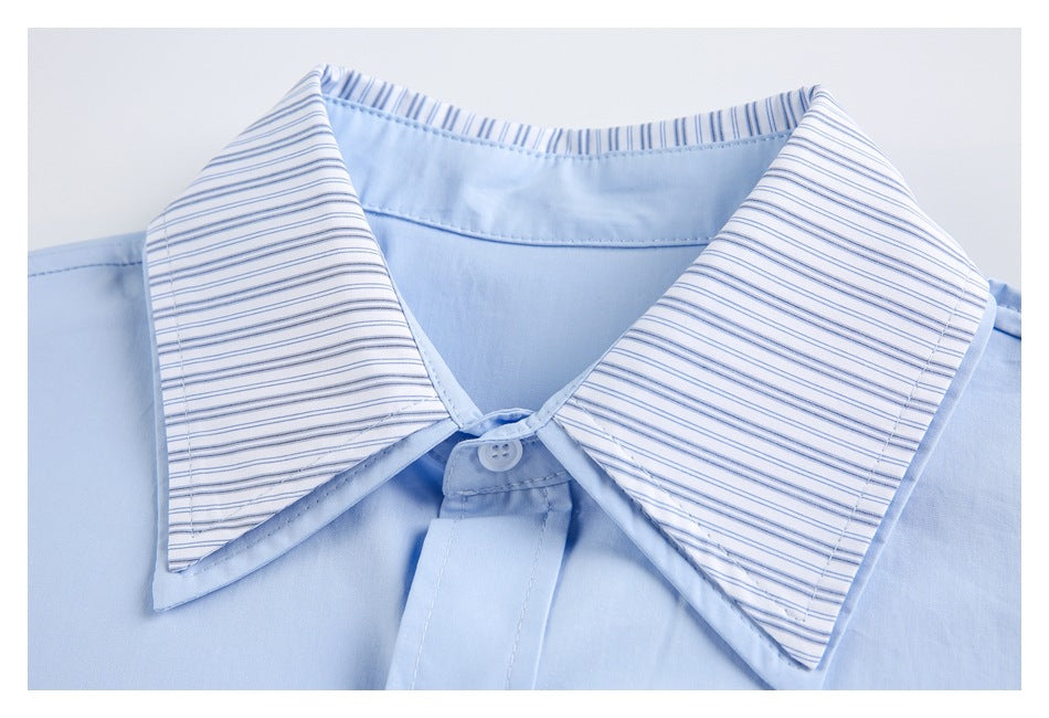Close-up of a light blue shirt with a wide blue-and-white striped collar and white buttons.