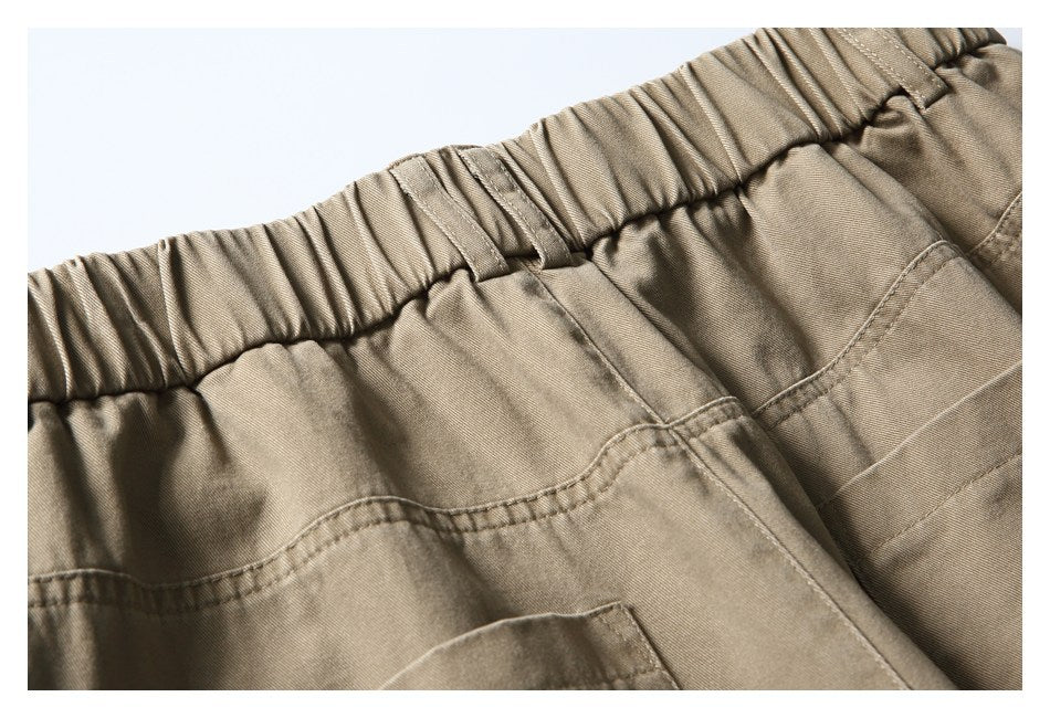 Close-up of khaki trousers with a gathered elastic waistband and stitched pockets.