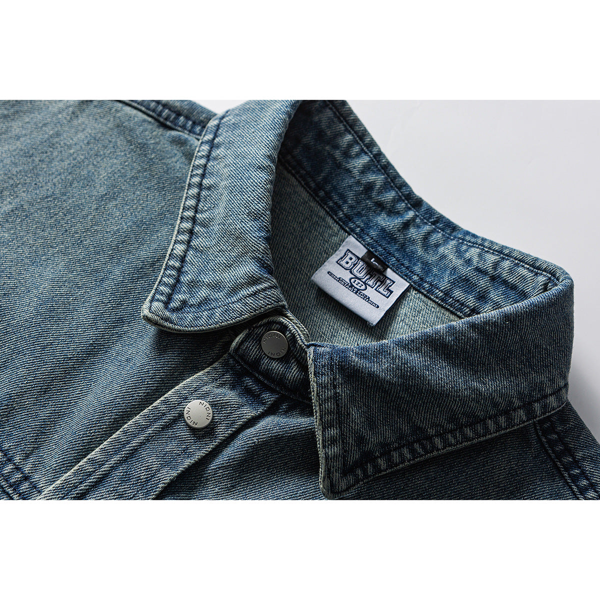 Close-up of a washed blue denim collar, metal buttons and sewn neck label.