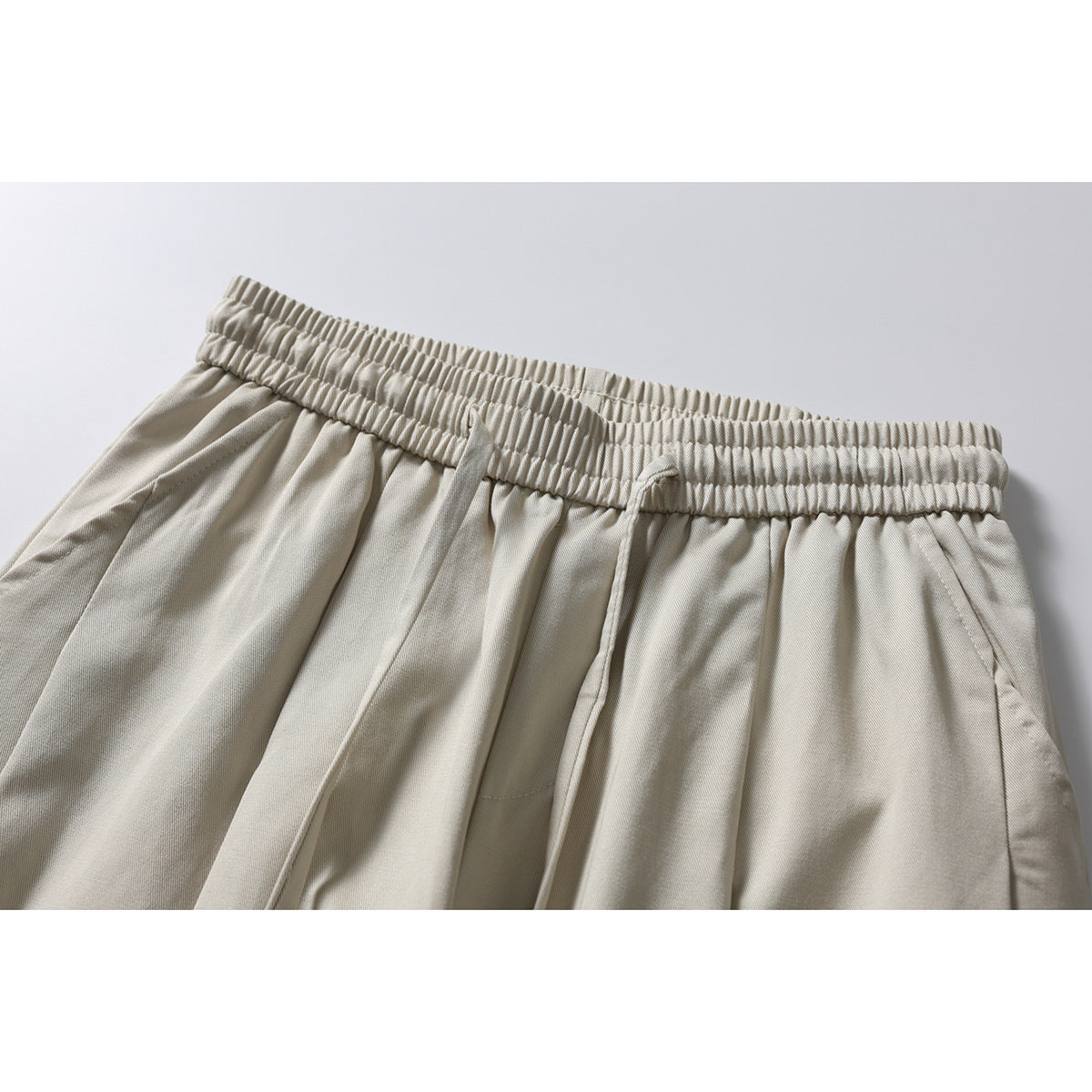Close-up of light beige wide-leg pants showing the gathered elastic waistband, drawstring, pleats and side pocket.