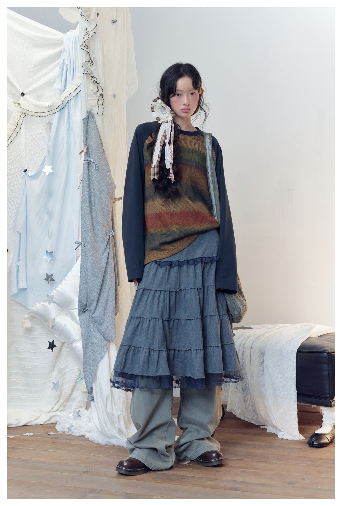 Model wearing a brown and muted multicolor striped top with navy sleeves, a gray tiered skirt and loose pants.