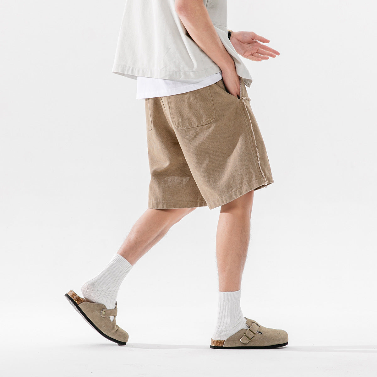 Side and rear view of a model wearing taupe shorts with a large back pocket and frayed side seam.