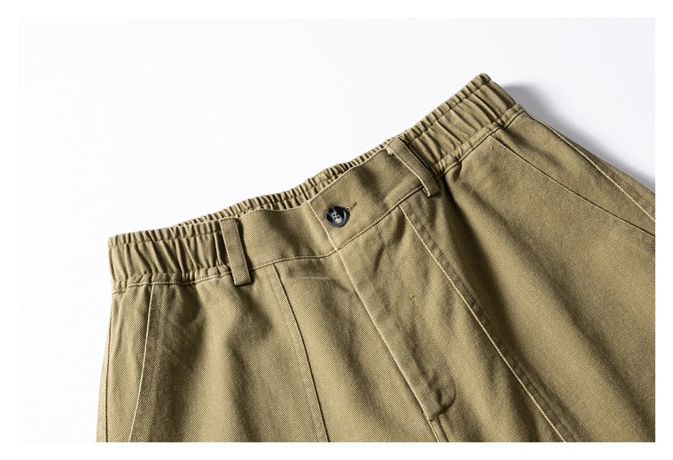 Close-up of olive-khaki shorts showing the elastic waistband, button, belt loops, and front seams.