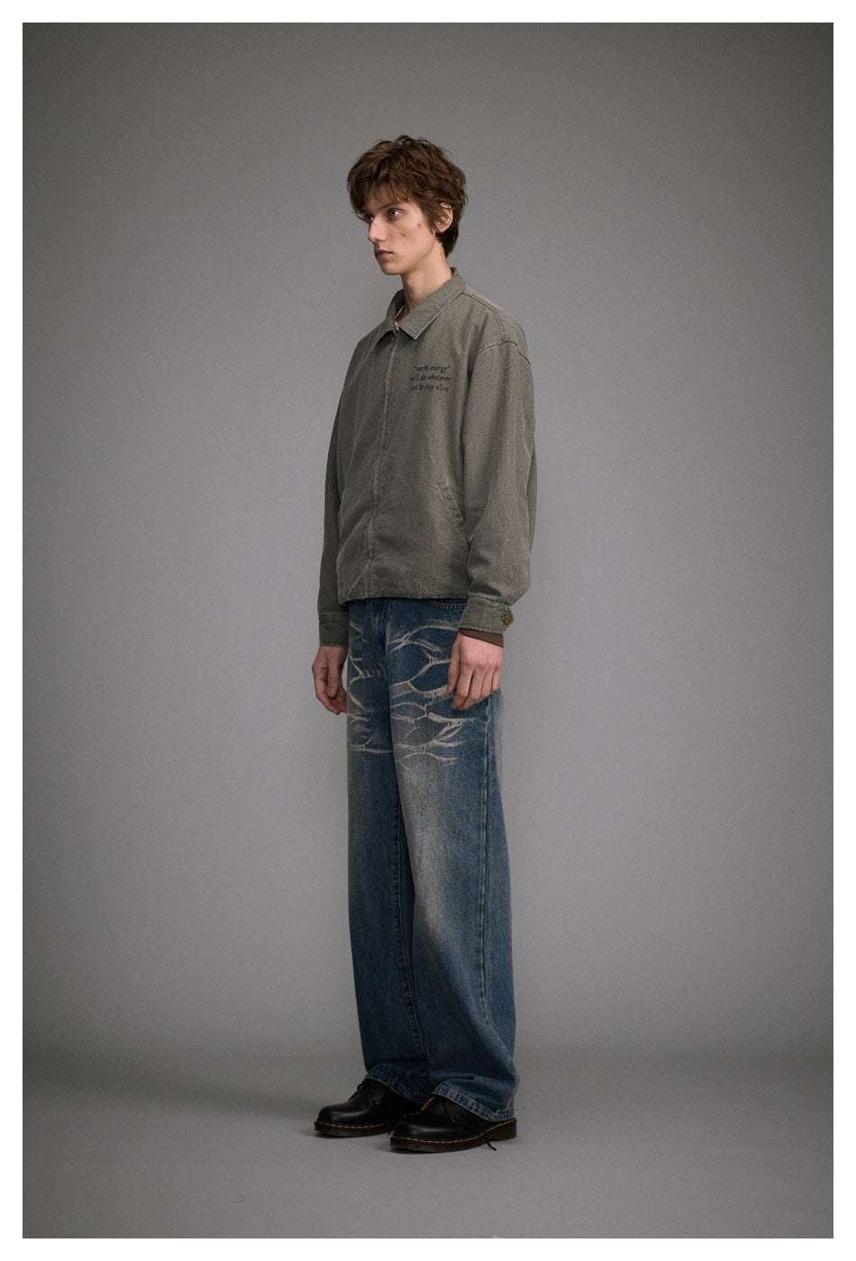 Model in side view wearing wide-leg washed blue jeans with a gray zip jacket and black boots