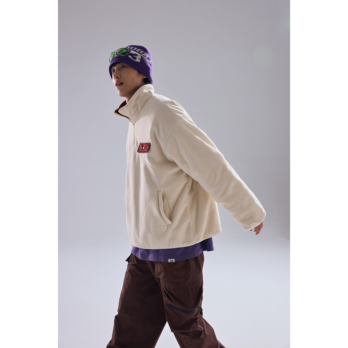 Model in a side view wearing an ivory quarter-zip pullover with burgundy chest pocket and brown cargo pants.