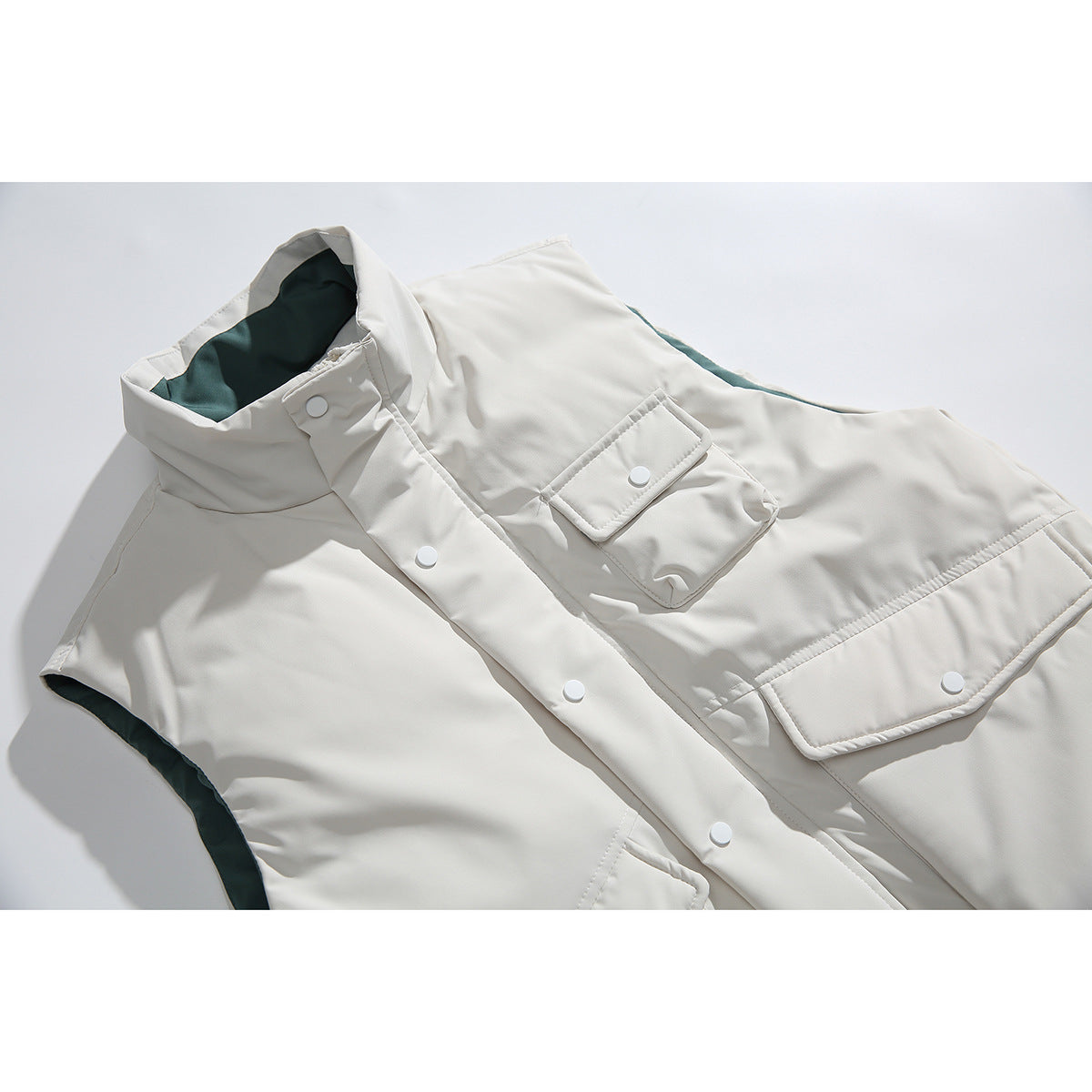Close-up of an ivory sleeveless vest showing its stand collar, snap-button placket, flap pockets and dark teal lining.