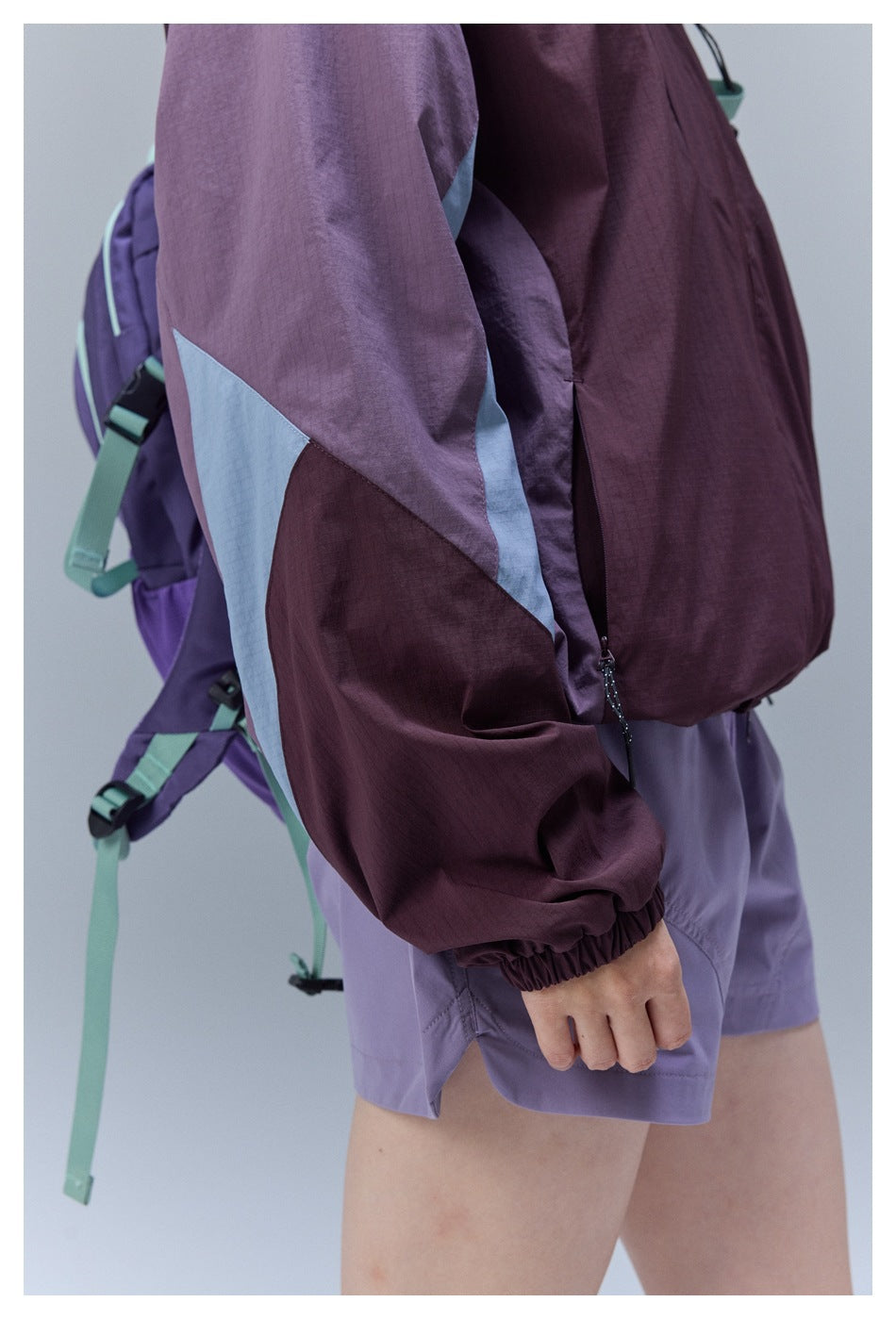 Close-up of the jacket's color-block sleeve, elastic cuff and side zipper, with lavender shorts visible.