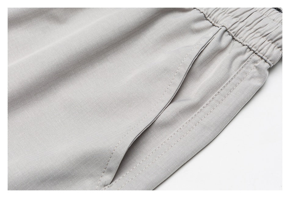 Close-up of a light-gray garment's elastic waistband and curved pocket opening with stitched edges.