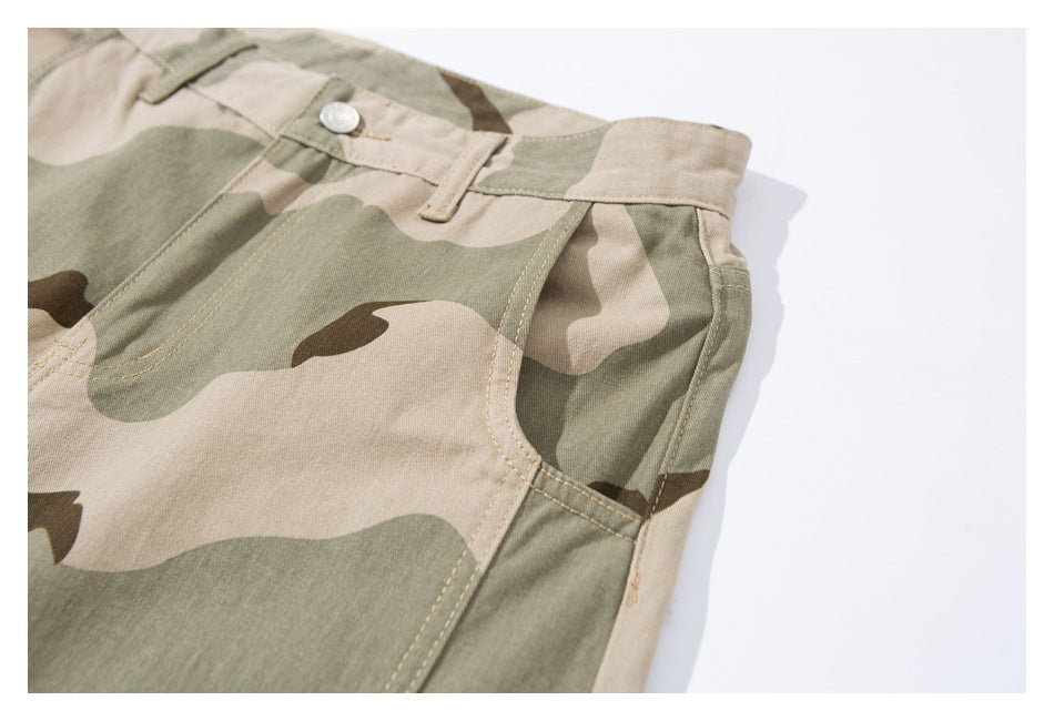 Angled close-up of the front waistband and curved pocket on beige, olive, and brown camouflage pants.