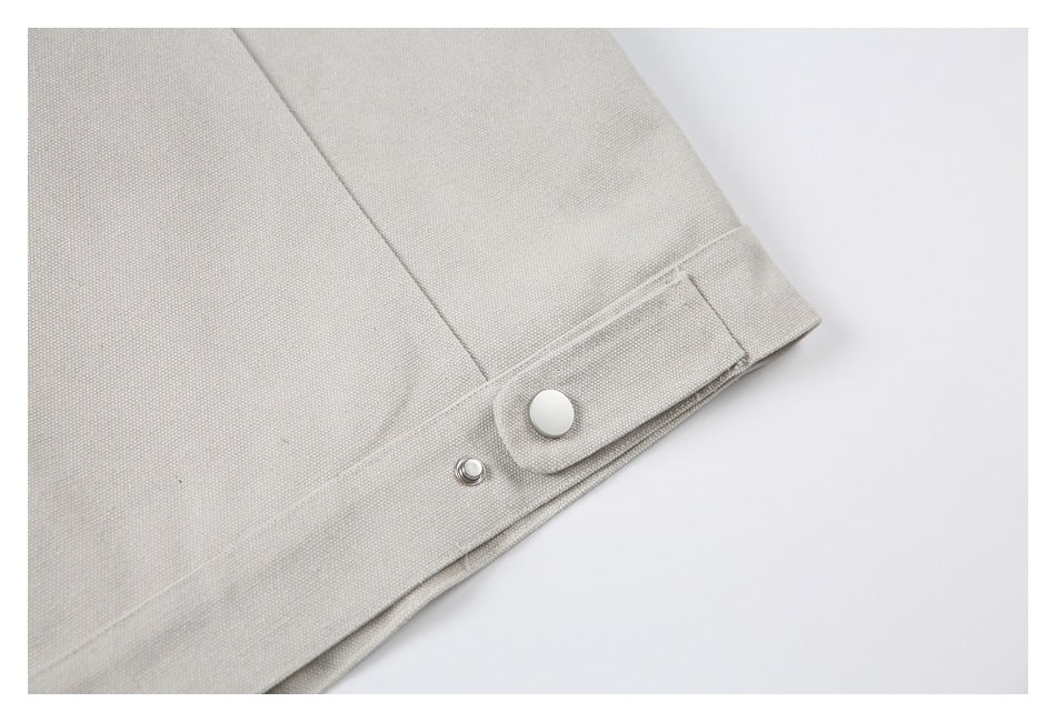 Close-up of a beige jacket hem tab with a round snap fastener.