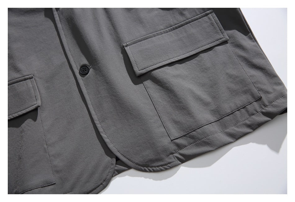 Close-up of a charcoal gray jacket front with large flap pockets, a dark button, and a curved hem.