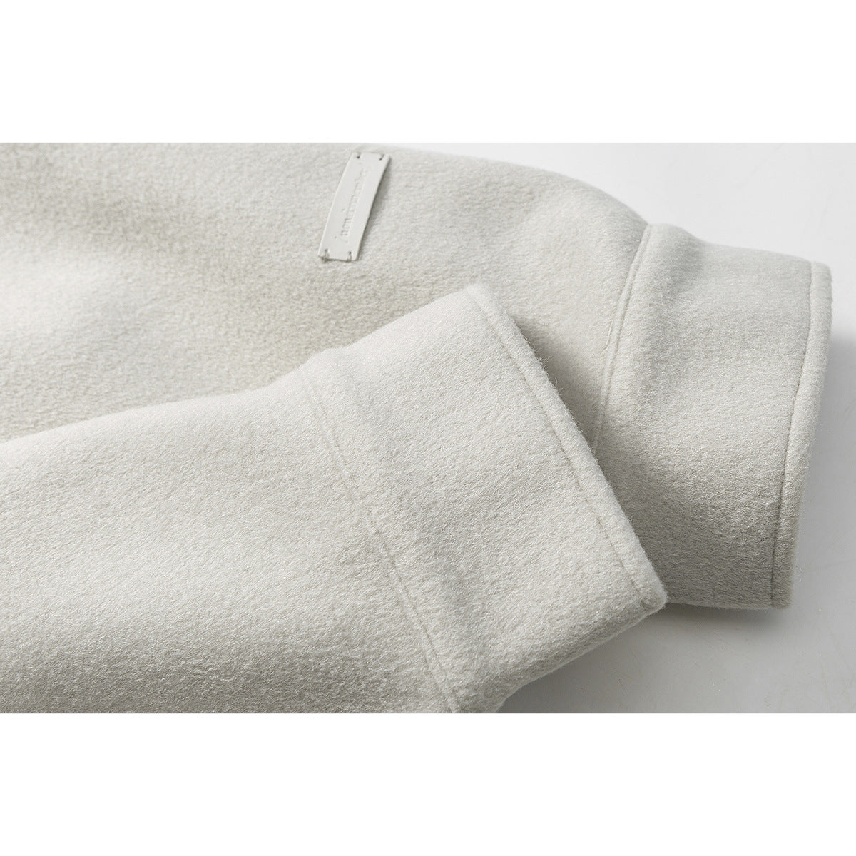 Close-up of an ivory coat sleeve, wide cuff, and small sewn label.