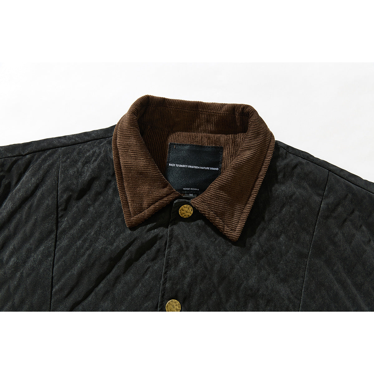 Close-up of a dark jacket collar in brown corduroy, with a brass-colored snap and sewn neck label.