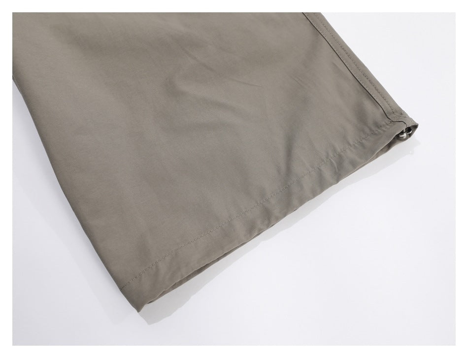 Close-up of the stitched hem and side seam at the leg opening of taupe trousers.