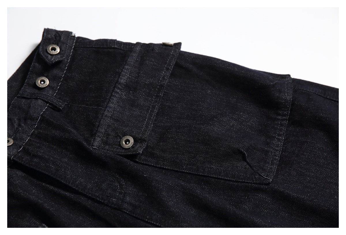 Black jeans laid flat, showing the waistband and a large buttoned flap pocket.