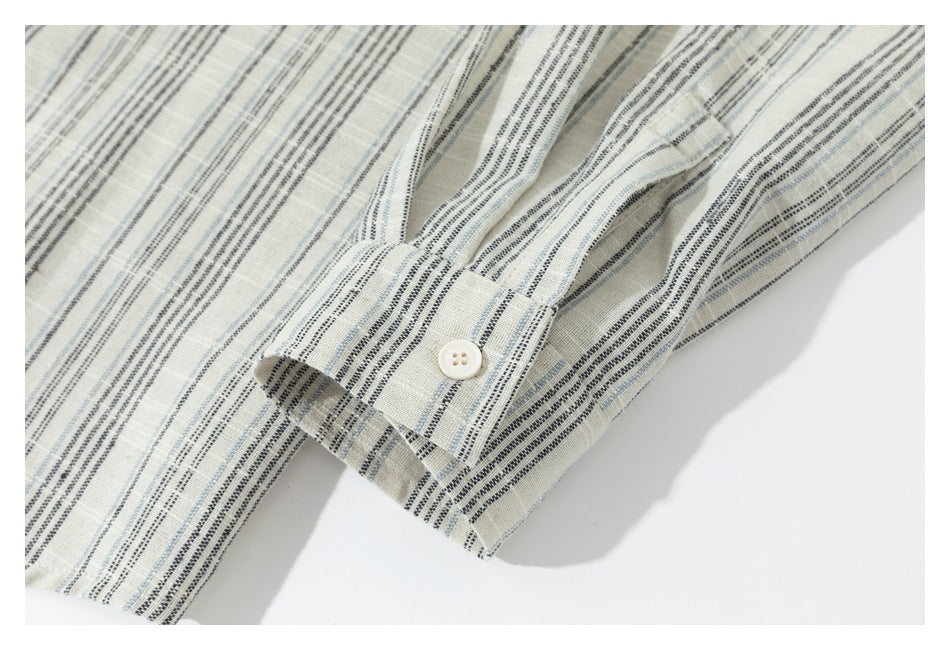 Close-up of a buttoned cuff on a cream shirt with black and pale blue stripes.