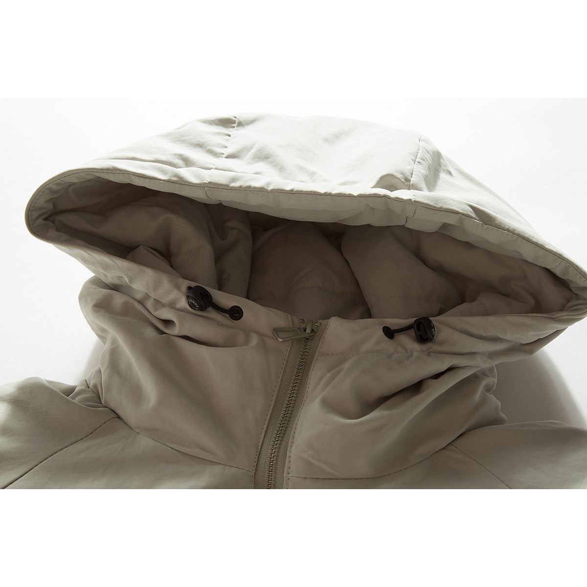 Close-up of a light beige hooded jacket showing the lined hood, drawcords, and front zipper.